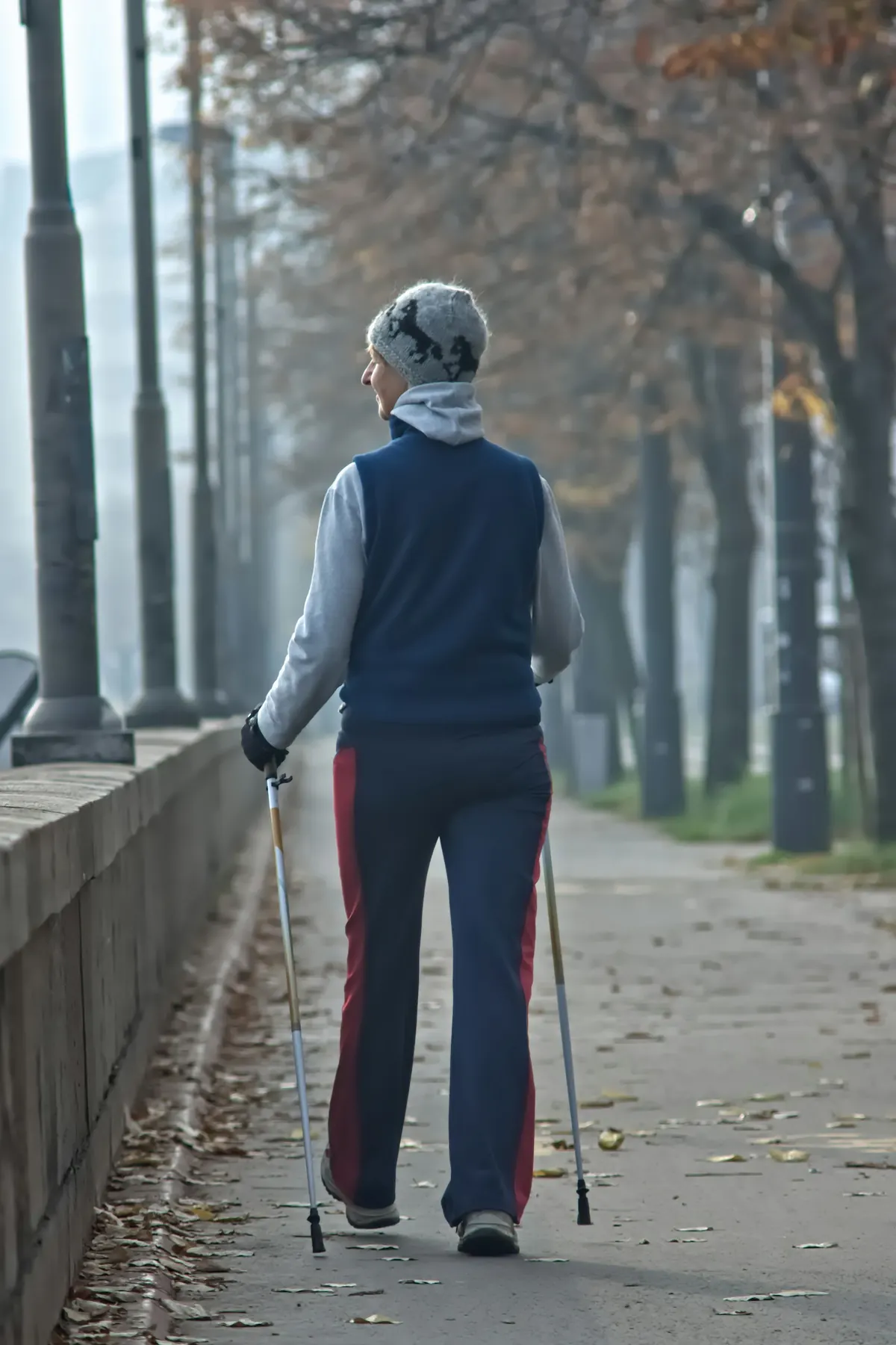 A woman walks with walking poles down a tree-lined path in autumn.